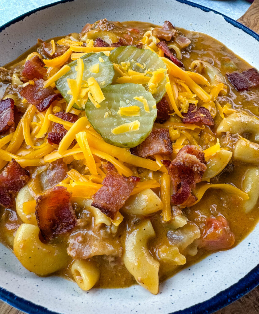 bacon cheeseburger soup with pickles and grated cheese in a white bowl