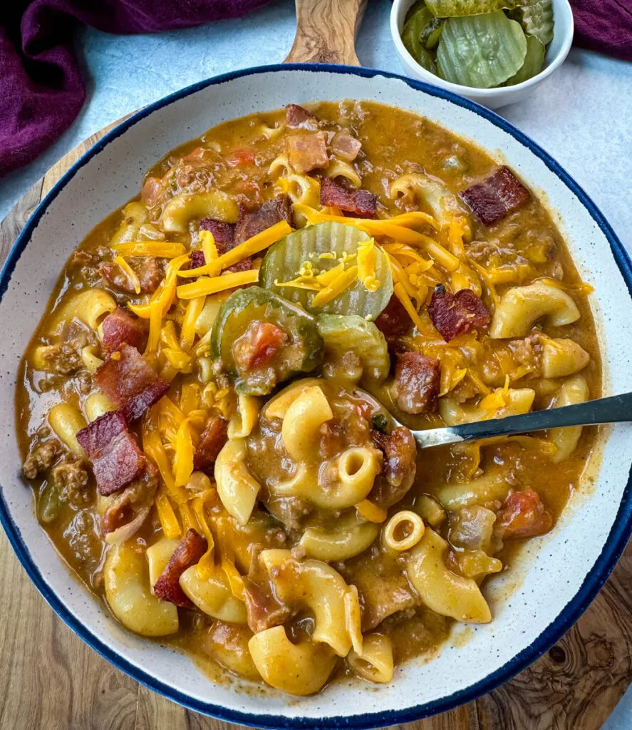 bacon cheeseburger soup with pickles and grated cheese in a white bowl