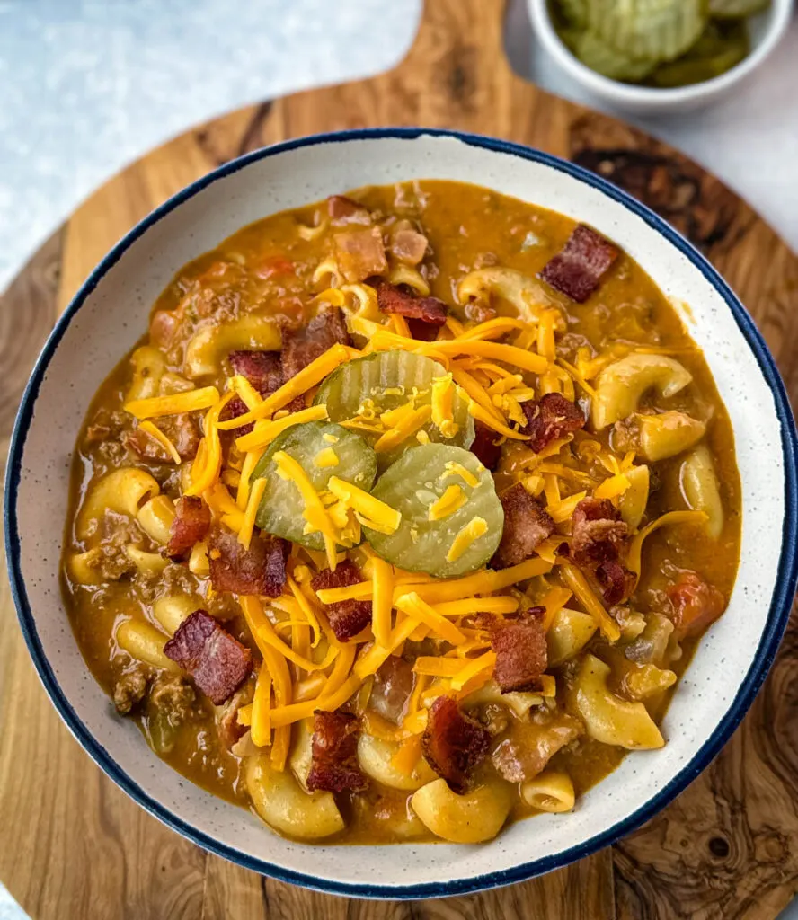 bacon cheeseburger soup with pickles and grated cheese in a white bowl