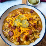 bacon cheeseburger soup with pickles and grated cheese in a white bowl