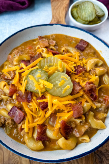 bacon cheeseburger soup with pickles and grated cheese in a white bowl