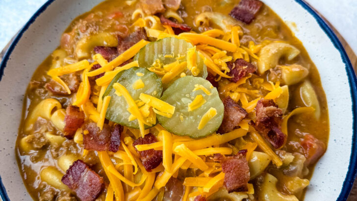 bacon cheeseburger soup with pickles and grated cheese in a white bowl