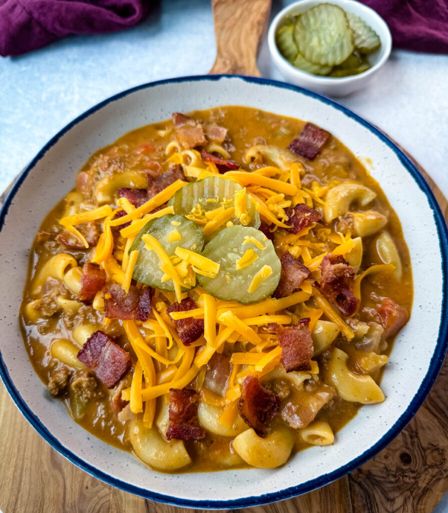 bacon cheeseburger soup with pickles and grated cheese in a white bowl