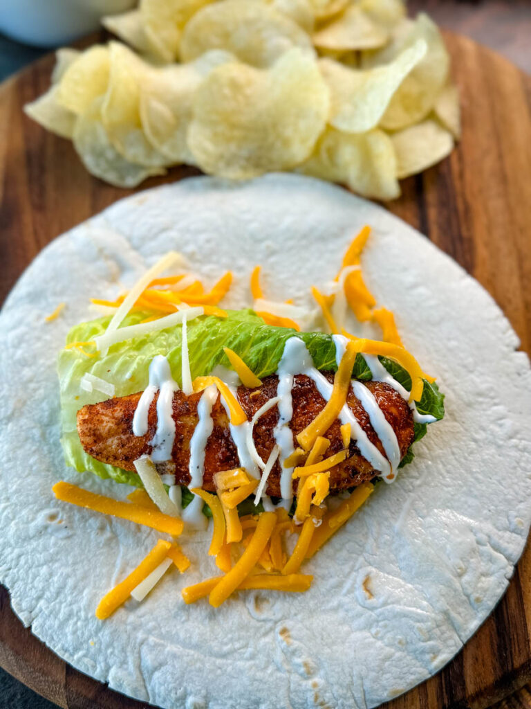 naked chicken tender on a tortilla with ranch dressing and shredded cheese