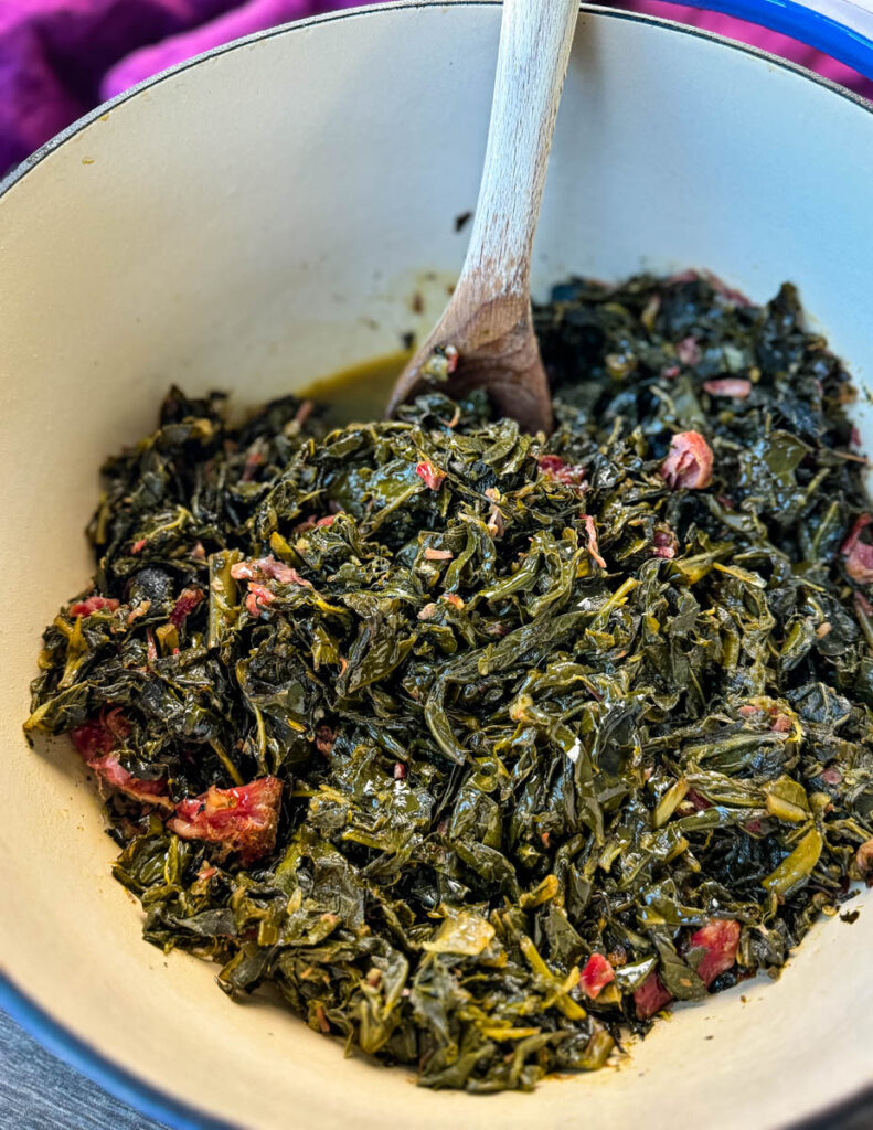 collard greens and ham hocks in a Dutch oven with a wooden spoon