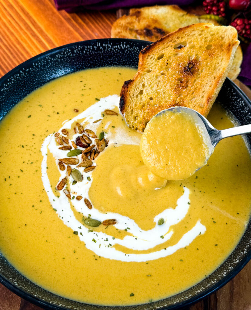 a spoonful of creamy butternut squash soup in a bowl with cream, nuts, and toasted bread