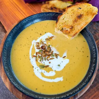 creamy butternut squash soup in a bowl with cream, nuts, and toasted bread