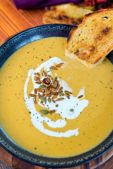 creamy butternut squash soup in a bowl with cream, nuts, and toasted bread