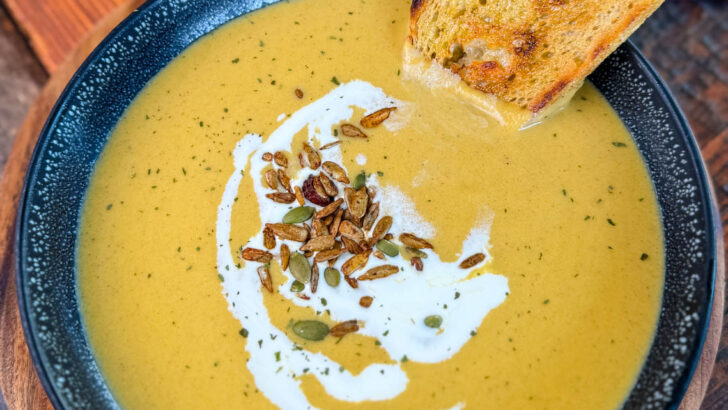 creamy butternut squash soup in a bowl with cream, nuts, and toasted bread