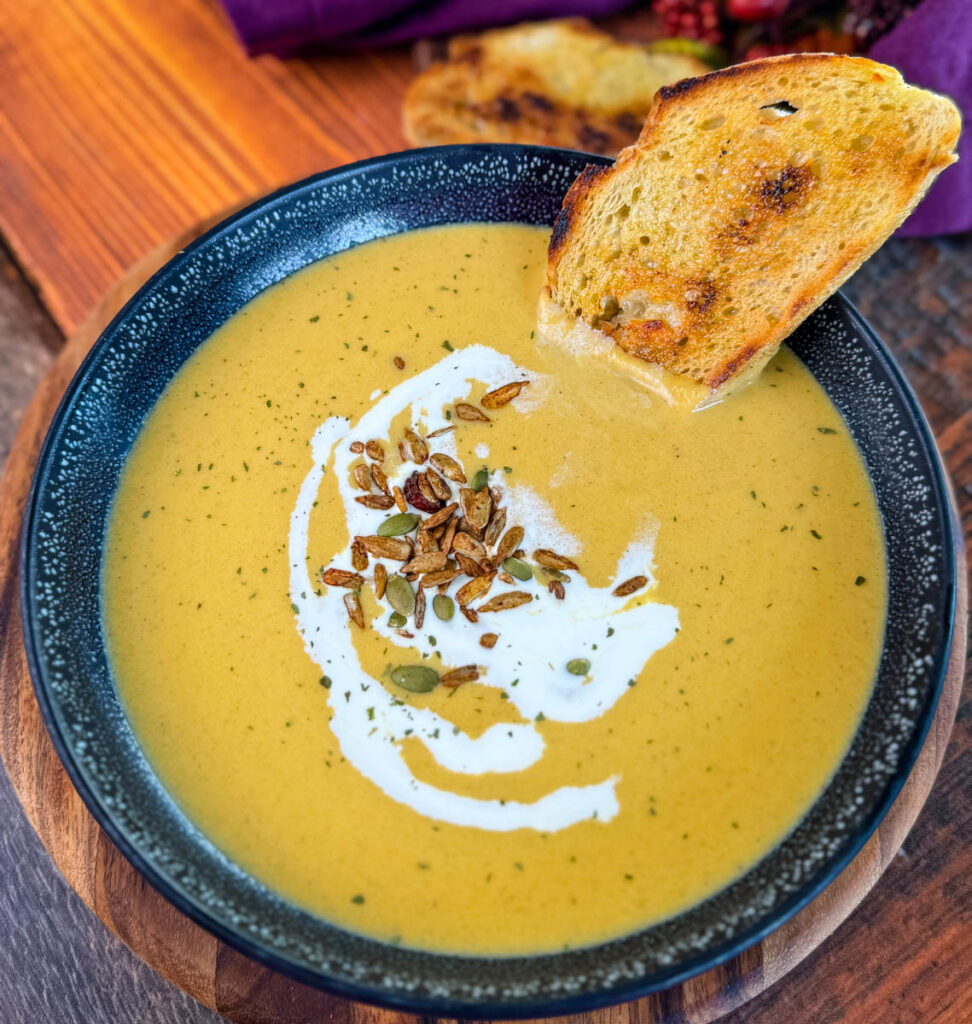 creamy butternut squash soup in a bowl with cream, nuts, and toasted bread