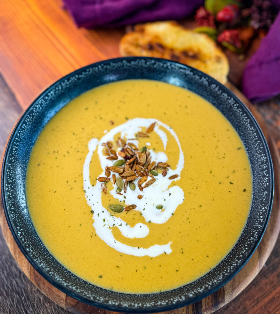 creamy butternut squash soup in a bowl with cream, nuts, and toasted bread