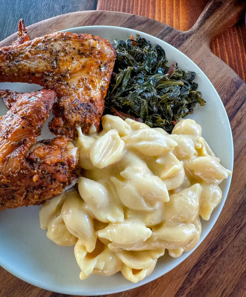 fried chicken wings, collard greens, and stovetop mac and cheese on a plate