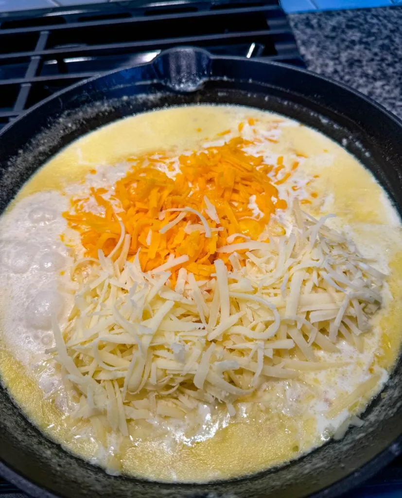 roux, cheese sauce, and grated cheddar cheese in a cast iron skillet