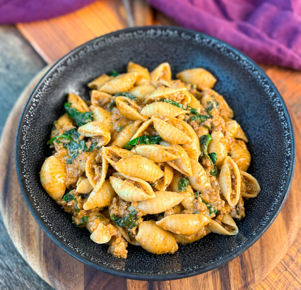 high protein beef and shells pasta with spinach in a black bowl