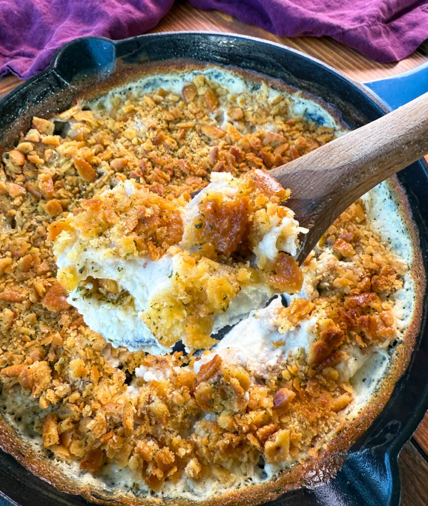 million dollar chicken casserole in a cast iron skillet with a wooden spoon