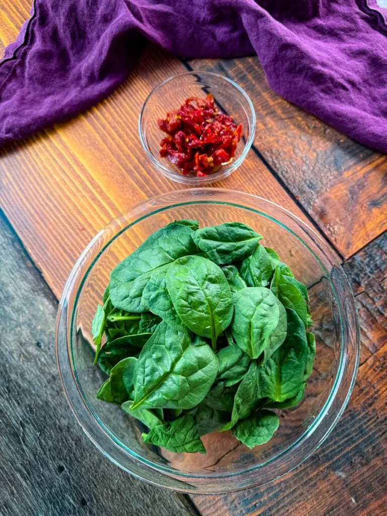 fresh spinach and sundried tomatoes in separate glass bowls