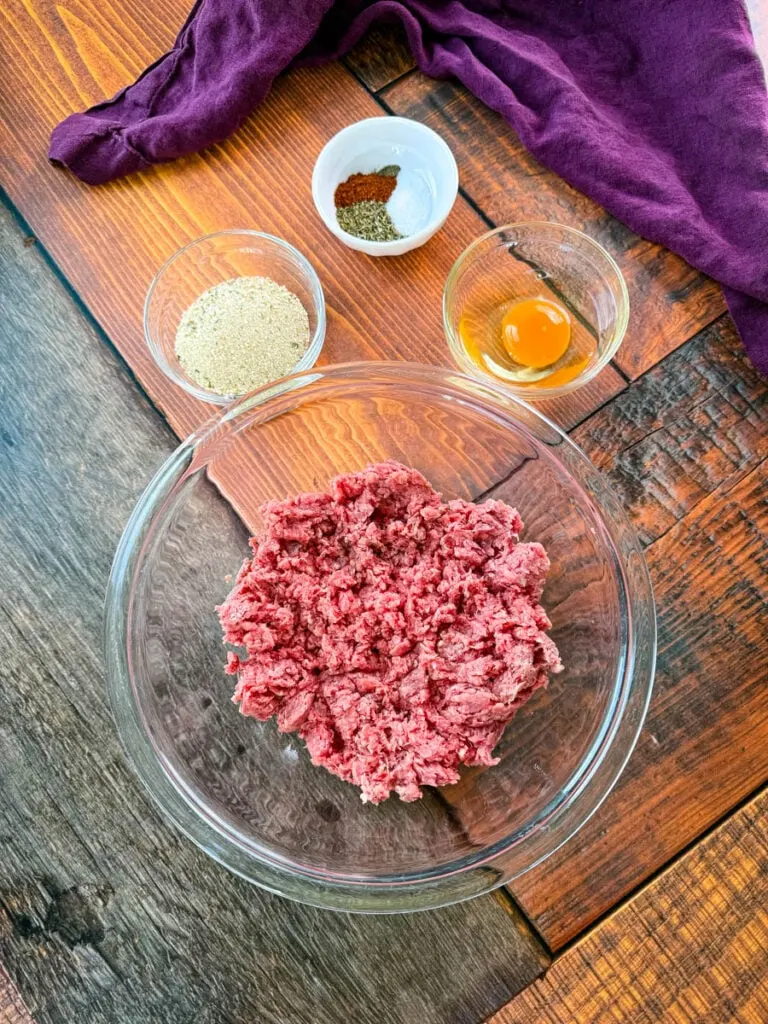 raw ground beef, breadcrumbs, egg, and spices in separate glass bowls