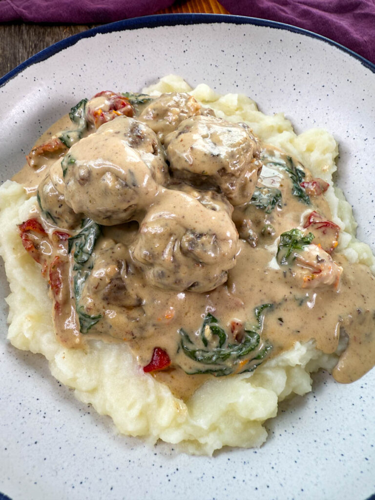 marry me meatballs drizzled in Tuscan cream sauce with mashed potatoes in a white bowl