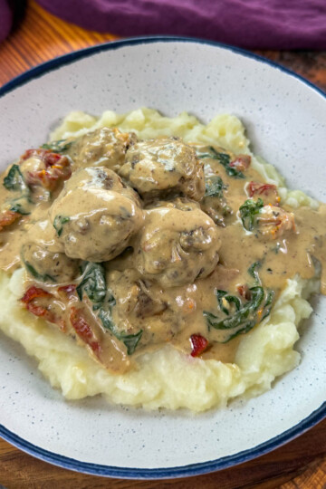 marry me meatballs drizzled in Tuscan cream sauce with mashed potatoes in a white bowl