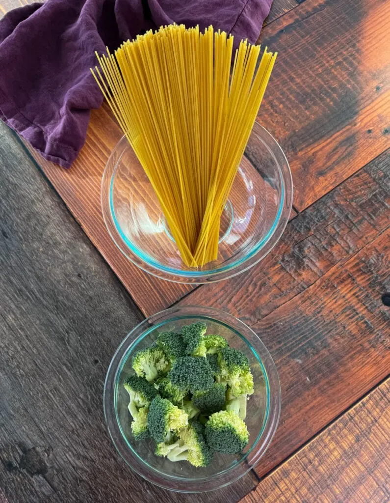 dry uncooked spaghetti pasta and fresh broccoli florets in separate glass bowls