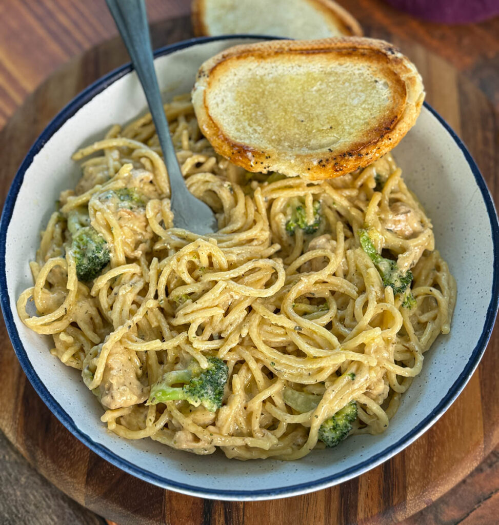 creamy chicken broccoli Alfredo in a white bowl with a fork and a piece of toasted bread