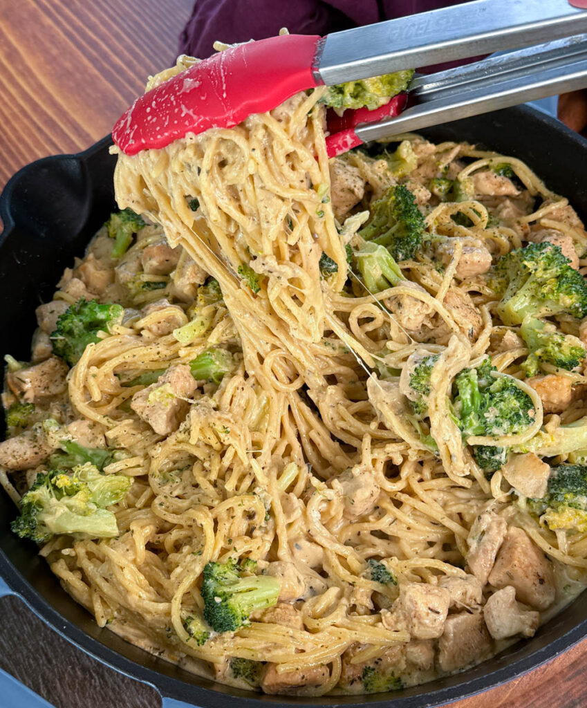 creamy chicken broccoli Alfredo with tongs in a skillet