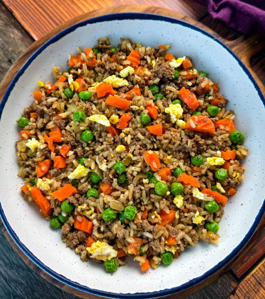 beef fried rice in a white bowl with eggs, peas, and carrots