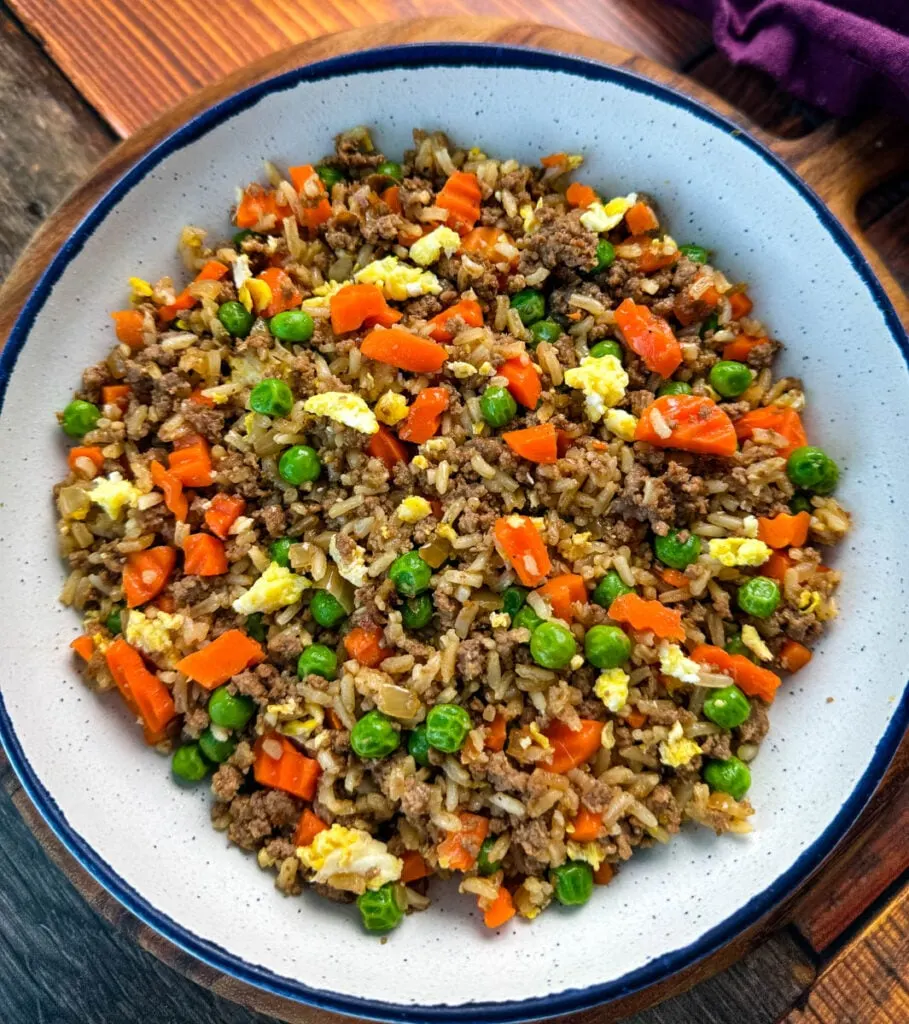 beef fried rice in a white bowl with eggs, peas, and carrots