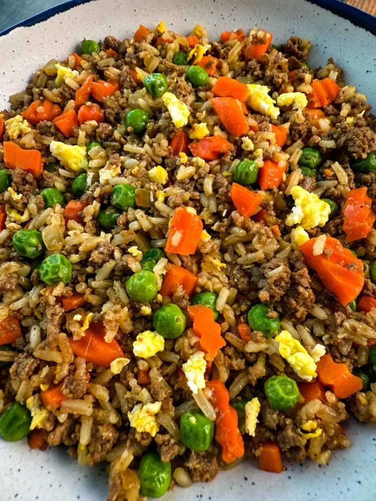 beef fried rice in a white bowl with eggs, peas, and carrots