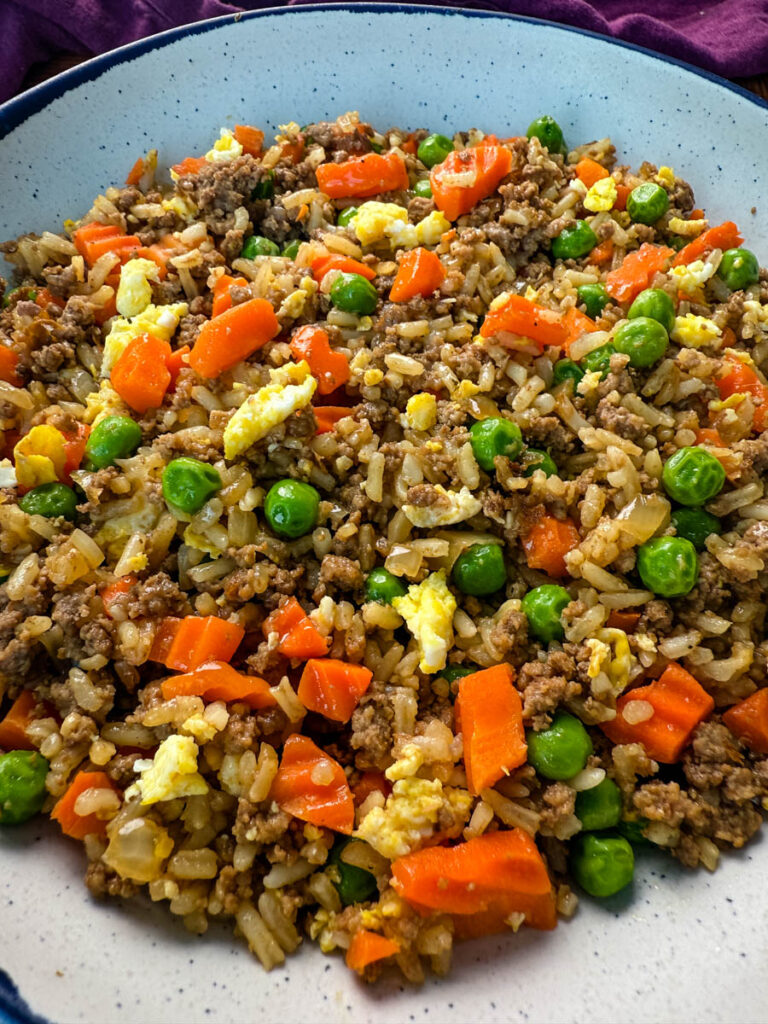 beef fried rice in a white bowl with eggs, peas, and carrots