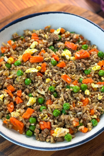 beef fried rice in a white bowl with eggs, peas, and carrots