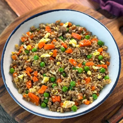 beef fried rice in a white bowl with eggs, peas, and carrots