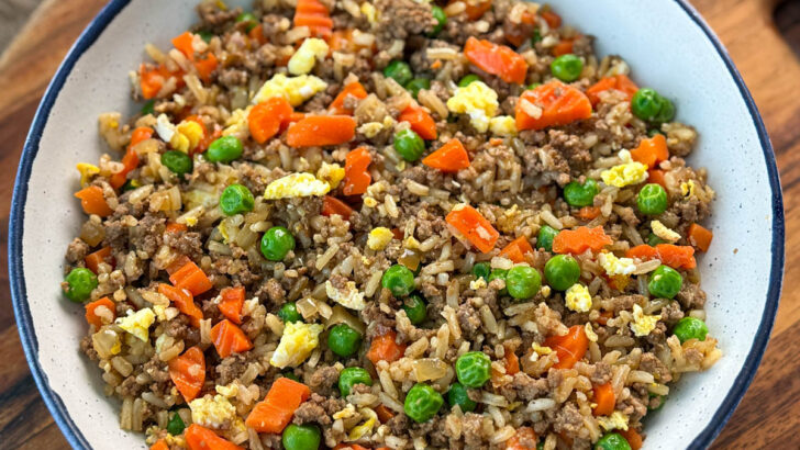 beef fried rice in a white bowl with eggs, peas, and carrots