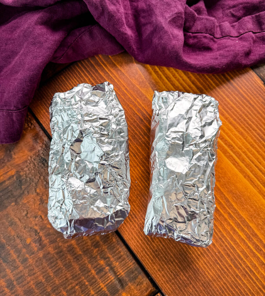 foil wrapped protein chicken burritos on a flat surface