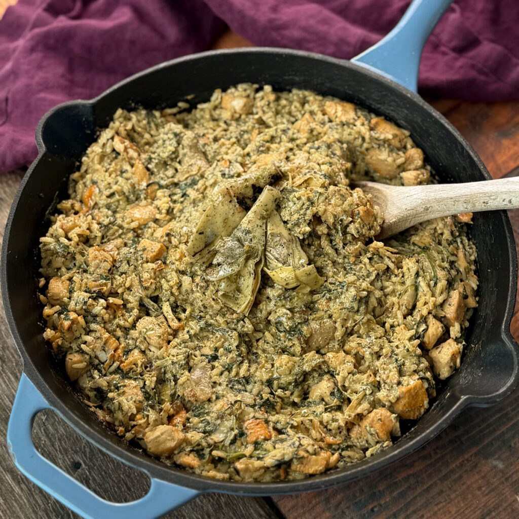 creamy spinach artichoke chicken and rice in a skillet with a wooden spoon