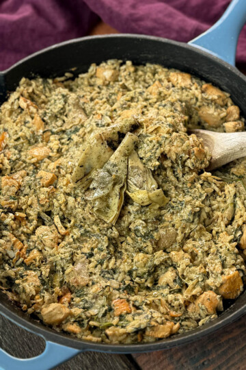 creamy spinach artichoke chicken and rice in a skillet with a wooden spoon