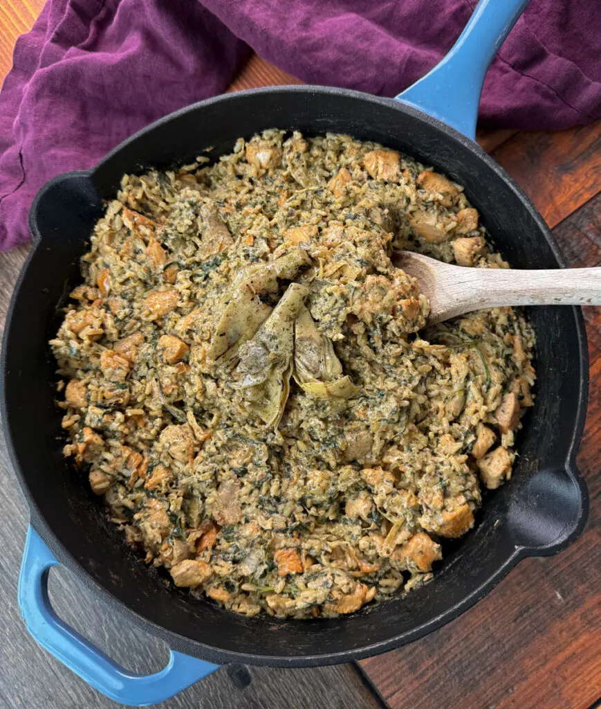 creamy spinach artichoke chicken and rice in a skillet with a wooden spoon