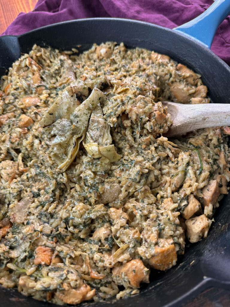 creamy spinach artichoke chicken and rice in a skillet with a wooden spoon