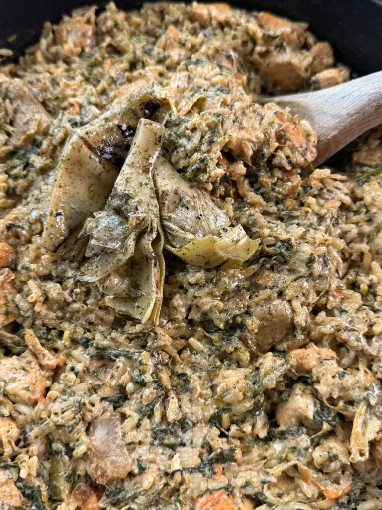 creamy spinach artichoke chicken and rice in a skillet with a wooden spoon