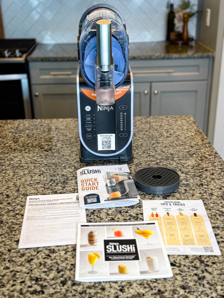 Unboxing of the Ninja SLUSHi Machine – The machine is displayed on a kitchen counter alongside instruction manuals, a recipe guide, and a quick start guide.