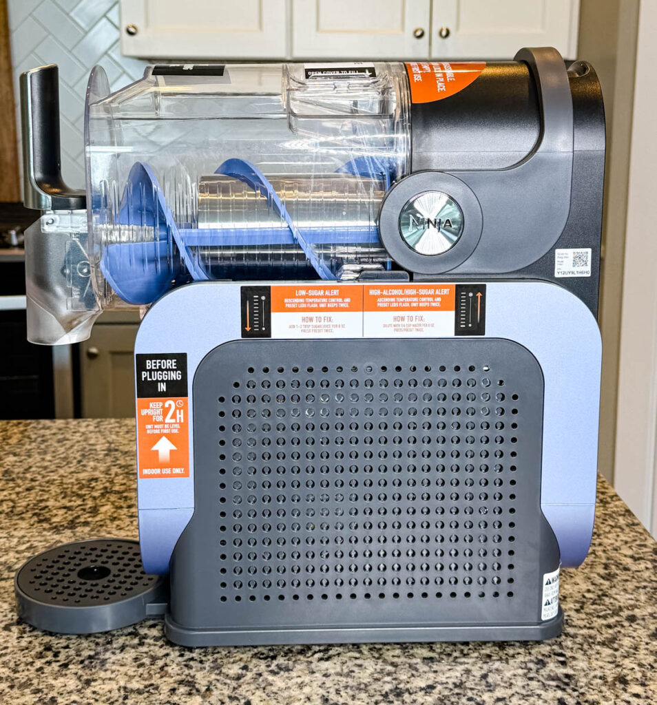 Empty Ninja SLUSHi Machine Side View – The chamber is empty, revealing the rotating auger inside. The machine is placed on a kitchen counter with a backsplash.