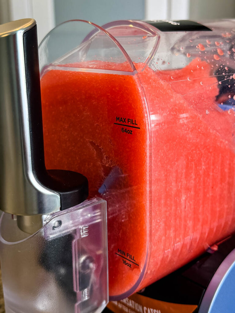 Close-up of the Ninja SLUSHi Machine’s Mixing Chamber – A transparent mixing chamber filled with bright red slush, showing the maximum and minimum fill lines on the side. The self-serve spout is visible in the foreground.