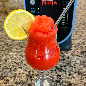 strawberry lemonade slushy in a glass with fresh lemon and a straw