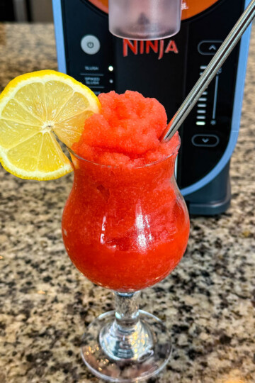 strawberry lemonade slushy in a glass with fresh lemon and a straw