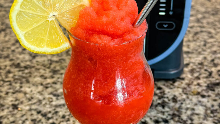 strawberry lemonade slushy in a glass with fresh lemon and a straw