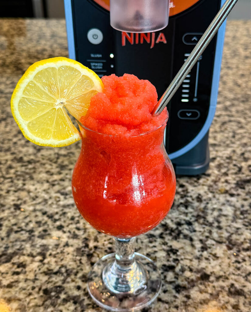 strawberry lemonade slushy in a glass with fresh lemon and a straw