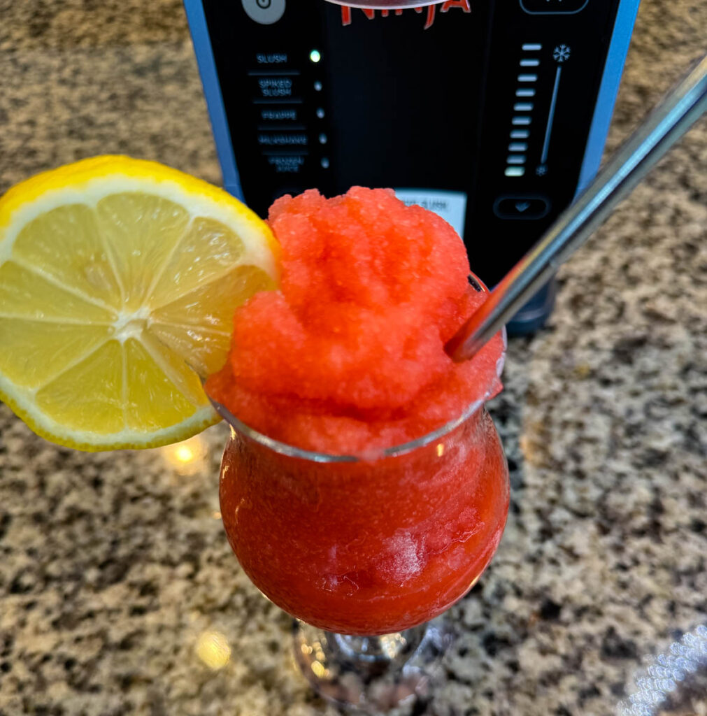 strawberry lemonade slushy in a glass with fresh lemon and a straw