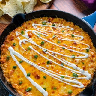 Hot and cheesy Buffalo Chicken Dip in a black cast-iron skillet, garnished with fresh green onions and a drizzle of ranch dressing, ready to be served.