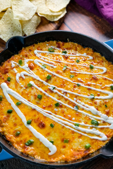 Hot and cheesy Buffalo Chicken Dip in a black cast-iron skillet, garnished with fresh green onions and a drizzle of ranch dressing, ready to be served.