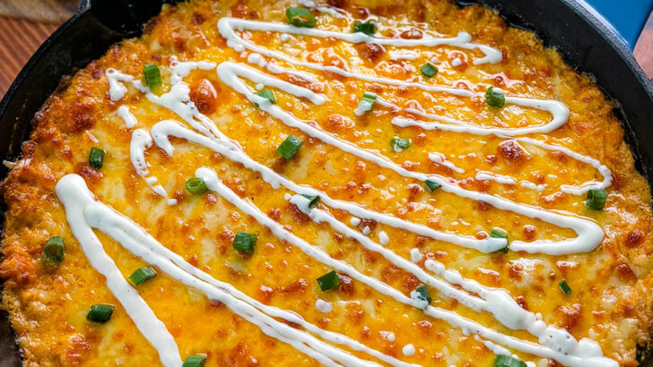 Hot and cheesy Buffalo Chicken Dip in a black cast-iron skillet, garnished with fresh green onions and a drizzle of ranch dressing, ready to be served.